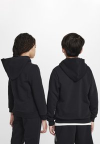 Felpe nere con cappuccio, realizzate in tessuto misto cotone, con polsini e orlo a coste, indossate da due bambini visti da dietro, mostrando un design minimal.