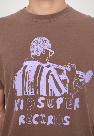 Rudas medvilninis T-shirt'as su violetiniu piešiniu, vaizduojančiu žmogų, grojantį trimitą, žemiau esantis tekstas "KID SUPER RECORDS".