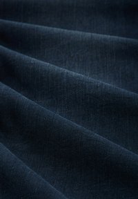 Tela de color azul oscuro con una textura suave, que presenta sutiles variaciones en el tono, caída en pliegues suaves, típica del material vaquero.