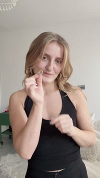 Boucles d'oreilles en métal doré et argenté exposées, présentant une forme géométrique unique. Le sujet tient les boucles d'oreilles devant un fond neutre.