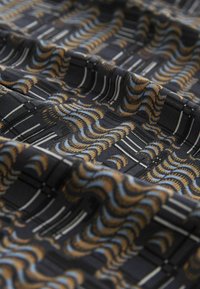 Tessuto nero con un motivo ondulato texturizzato in oro, blu e bianco. Presenta linee orizzontali e un aspetto complessivo levigato.