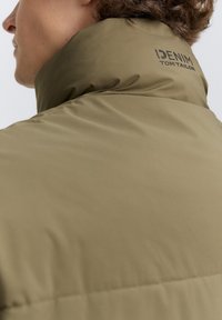 Olivengrøn polstret jakke med høj krave, prydet med brandlogoet "DENIM TOM TAILOR" i sort på bagsiden, glat stofstruktur.