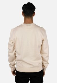 Sudadera beige claro con cuello redondo, mangas largas y puños y dobladillo acanalados. Textura suave con detalles de diseño mínimos.