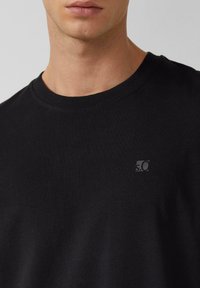 Zwarte katoenen T-shirt met een ronde hals, voorzien van een klein grijs logo op de borst. Glad textuur en casual pasvorm.