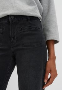 Jean en denim noir avec une coupe slim, taille mi-haute, design à cinq poches et une texture lisse, accompagné d'un haut à manches longues gris.