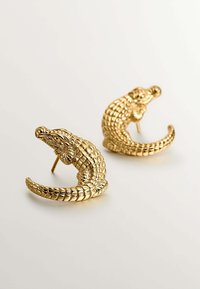 Pendientes en forma de cocodrilo dorados que presentan una superficie texturizada con un intrincado detalle, mostrando un diseño de cola rizada para un aspecto distintivo.