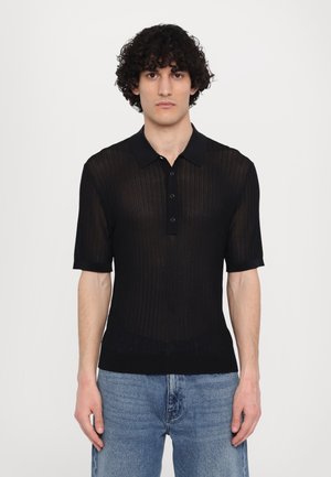 Camisa polo preta de manga curta com textura ribateada, abertura com três botões e colarinho. Combinada com jeans azul.