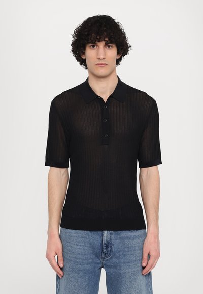 Polo shirt noir à manches courtes avec une texture côtelée, un plastron à trois boutons et un col. Assorti à un jean en denim bleu.