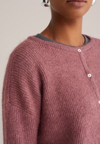 Pletený cardigan z měkké růžové vlněné směsi, s kulatým výstřihem, dlouhými rukávy a bílými knoflíky na přední straně. Strukturovaný povrch.