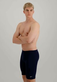 Shorts de bain de sport en navy avec une texture lisse, ajustés près du corps, présentant un petit logo Nike blanc sur la jambe gauche.