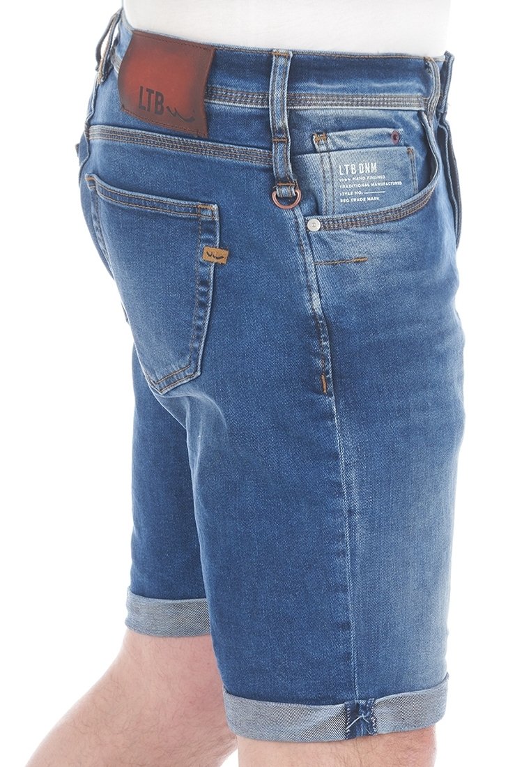 Short en jean avec revers roulés, coutures visibles, écusson de marque en cuir marron à la taille et petite étiquette en tissu sur la poche arrière.