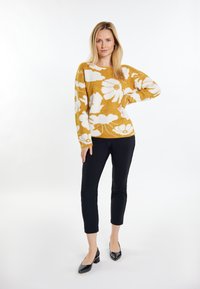 Maglione floreale giallo con motivi a fiori bianchi, vestibilità comoda, scollatura tonda. Abbinato a pantaloni neri slim-fit e ballerine nere a punta.