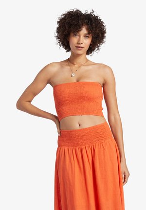 Orange cropped strapless top with smocked texture, paired with a matching long skirt featuring a smocked waistband. Smooth fabric.