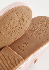 Semelles de chaussures roses avec motif en relief de chaussures de ballet et d’étoiles, taille 6F, et nom de marque Next visible sur la semelle.