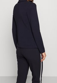 Navy long-sleeve top with a collar, soft texture, and a fitted design, paired with matching pants featuring white side stripes.