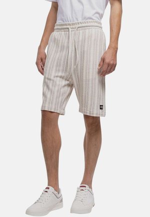 Homme portant un short en tricot beige rayé avec taille à cordon, des baskets blanches et un t-shirt blanc, se tenant les mains détendues le long du corps.