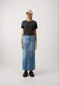 Black T-shirt, denim maxi skirt with patchwork design, light blue shade, textured surface, paired with thick-soled black shoes and a beige cap.