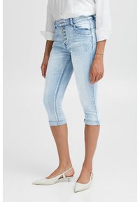 Pantalones capri de mezclilla azul claro con un diseño ajustado, cierre de cinco botones y dobladillos enrollados. Textura suave, detalles de costura clásicos.
