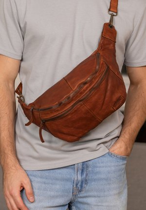 Braune Leder-Schultertasche mit geschwungener Form, Reißverschlusstaschen und verstellbarem Trageriemen. Strukturiere Oberfläche und leichtes Glänzen.