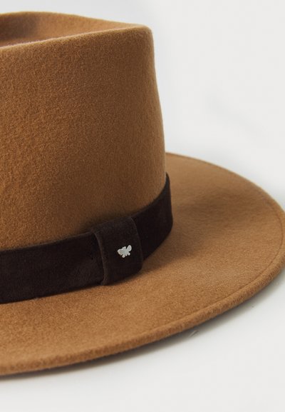 Chapeau en feutre marron à large bord, orné d'un bandeau en daim noir et d'un emblème en argent représentant une abeille sur le côté. Texture douce, design structuré.