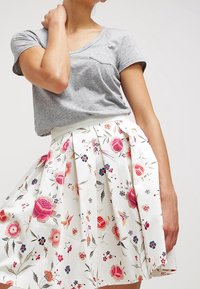 Graues T-Shirt mit kurzen Ärmeln, kombiniert mit einem hoch taillierten weißen Faltenrock, der ein floral bedrucktes Muster in Pink, Rot, Blau und Grün aufweist.