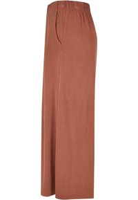 Pantalon large couleur terre cuite en tissu doux et texturé avec une ceinture élastique et des poches latérales. Design simple, coupe longue.