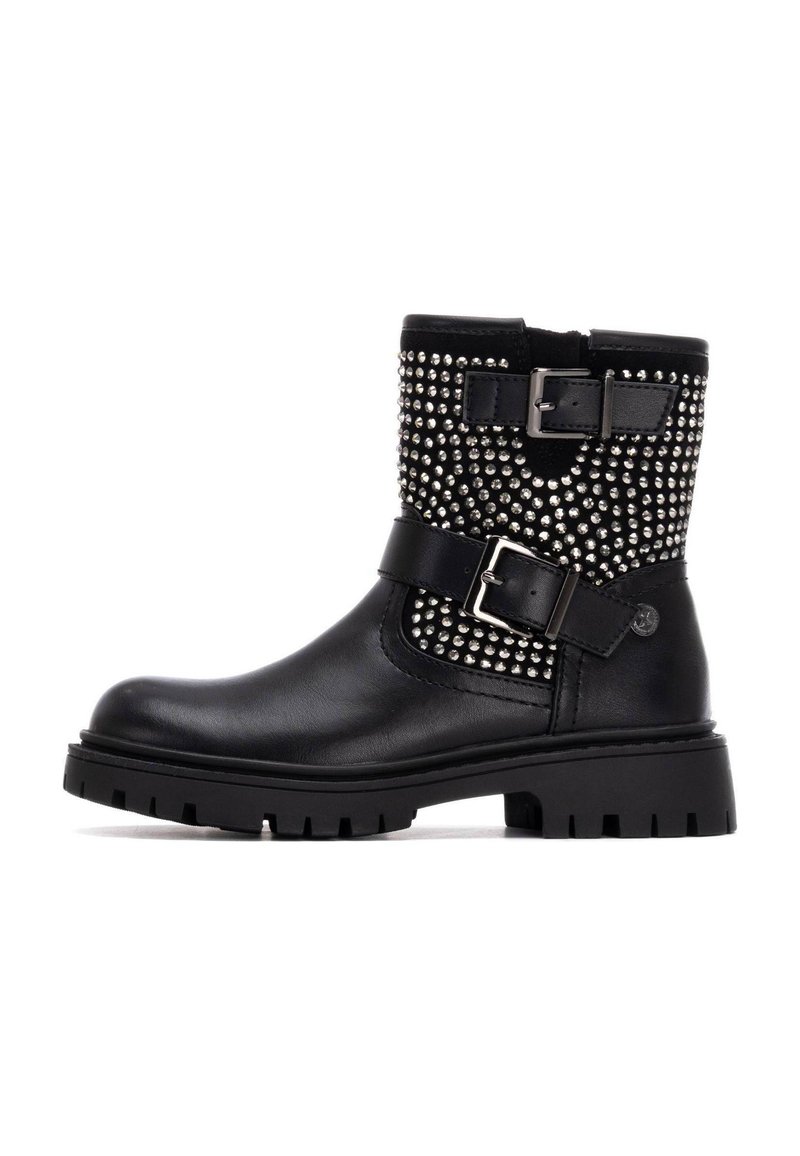Bottine en cuir noir avec un design à clous, semelle en caoutchouc plate, sangle à boucle ajustable et détail texturé sur le dessus.
