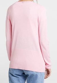 Pull en maille rose avec un ourlet côtelé, des manches longues et un col rond. Texture douce et tissu léger.