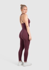 Bordeaux sportieve jumpsuit met een nauwsluitend ontwerp, dunne gekruiste banden en een zachte textuur. De leggings zijn full-length en hoog in de taille.