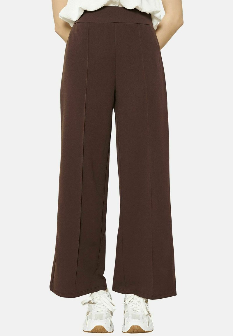 Pantalons amples marron en tissu doux, avec une taille haute, deux plis à l'avant, portés avec des baskets blanches.