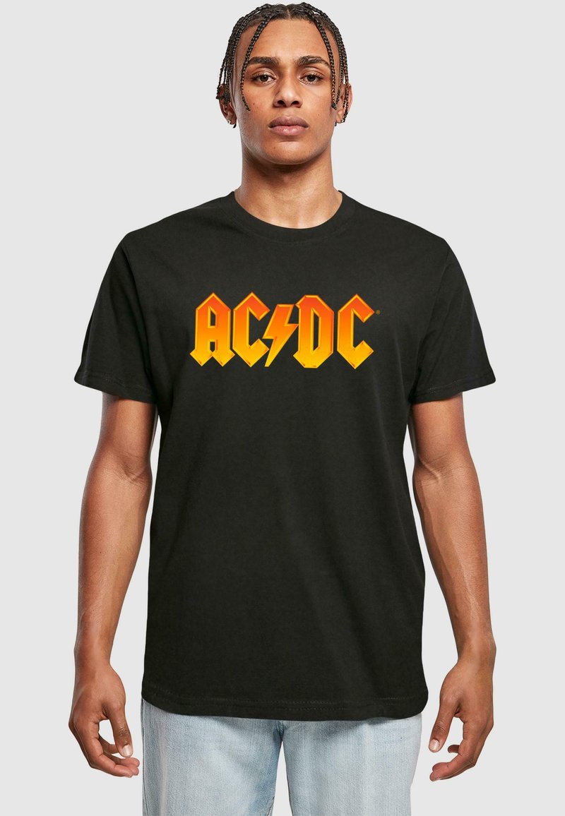 Juodas medvilnės marškinėlis su ryškiai oranžine ir geltona AC/DC logotipu per krūtinę, apvaliu iškirpimu ir trumpomis rankovėmis.