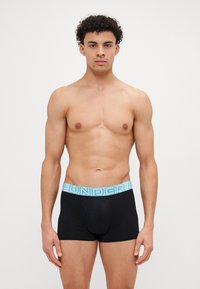 Sorte boksershorts med en lyseblå elastisk linning som har teksten "UNDER" i fet skrift. Glatt stoff, tettsittende design og midt på låret lengde.