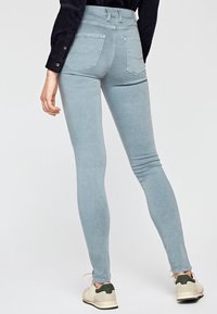 Vaqueros skinny de un azul claro con cintura alta, bolsillos traseros y una textura suave, combinados con zapatillas beige con acentos verdes.
