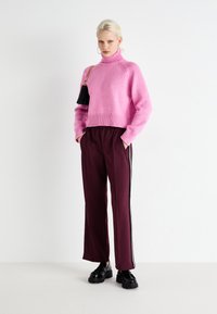 Pink knit sweater with a high collar, paired with burgundy pants featuring side stripes, and black platform shoes. Handbag with chain strap.