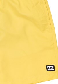 Gele zwemshorts van lichtgewicht stof, met een gestikte zoom en een zwart logo-label op de linkeronderkant. Soepele textuur.