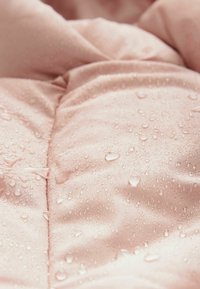 Wasserabweisender rosa Stoff mit glatter Textur, der Tropfen auf der Oberfläche und gestickte Muster für zusätzliche Designmerkmale aufweist.