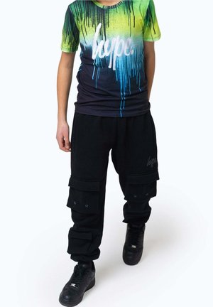 Enfant portant un pantalon cargo noir et un t-shirt dégradé du vert au bleu avec le texte « hype. », marchant sur un fond blanc.