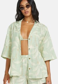 Camicia button-up verde menta con motivo a foglia di palma, maniche corte e vestibilità comoda, abbinata a un bikini top coordinato.