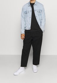 Ljusblå denimjacka med två framfickor, över en svart t-shirt, i kombination med svarta lösa byxor och vita sneakers. Enkelt design.