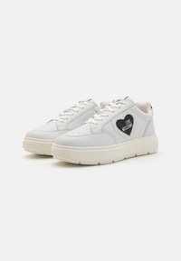 White leather sneakers featuring a black heart patch with "LOVE MOSCHINO" text, round toe, lace-up design, and cream rubber sole.