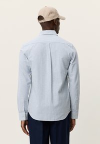 Ανοιχτό μπλε ριγέ πουκάμισο με μανσέτες με κουμπιά και καμπυλωτή κάτω όψη. Κατασκευασμένο από βαμβακερό ύφασμα, διαθέτει πίσω καβάλο και μονή πιέτα στο κέντρο.