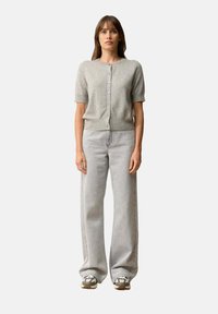 Szary dziergany kardigan z krótkimi rękawami i guzikami z przodu, zestawiony z jasnoszarymi spodniami z szerokimi nogawkami oraz wzorzystymi trampkami.