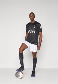 Maglia da calcio nera con logo AIA ed emblema del club, pantaloni corti bianchi, calze nere, scarpini neri e un pallone da calcio con motivo ai piedi.