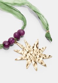 Pendente a forma di stella dorata con una texture martellata, accompagnato da tre perline viola su un nastro verde trasparente.