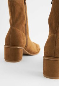 Botine negre din suede cu fermoar, formă conturată și toc mediu, pătrat. Materialul are un finisaj moale, texturat.