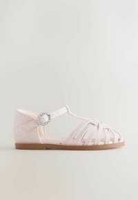 Sandale rose scintillante avec un design à lanières, boucle réglable et semelle souple. Elle présente un bout rond et une semelle extérieure plate et flexible.
