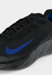 Μαύρο δρομικό παπούτσι Nike με μπλε λογότυπο swoosh, υφασμένο πέλμα και μαύρα κορδόνια.