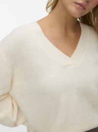 Krémově zbarvený svetr z pleteniny se zaobleným výstřihem do V, volným střihem a texturovanou látkou. Má žebrované detaily podél výstřihu.