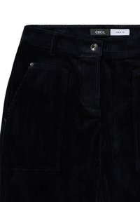 Marineblaue Cordhosen mit vertikaler gerippter Textur, ausgestattet mit vorderen Taschen und einem Metallknopfverschluss. Etikett trägt den Aufdruck "CECIL PANTS".