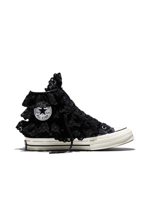 Zapatilla Converse de caña alta en negro con volantes de encaje negro superpuestos y suela de goma blanca, vista de lado sobre un fondo blanco.